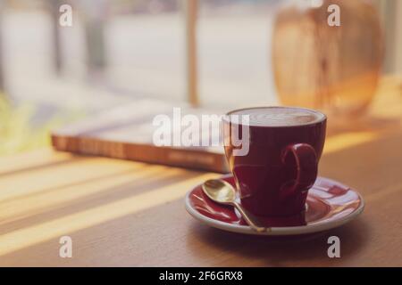 Gros plan Latte art chaud, Cappuccino café dans une tasse rouge sur une table en bois dans un café arrière-plan flou avec le processus d'image bokeh avec style vintage Banque D'Images