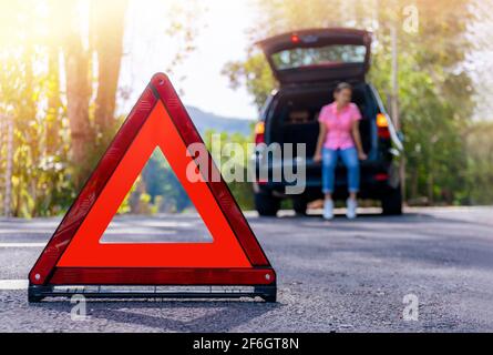 Gros plan sur le panneau rouge d'arrêt d'urgence sur la route. Femme inquiète et en colère marchant près de sa voiture cassée parlant au téléphone avec l'agent d'assurance. Gros plan Banque D'Images