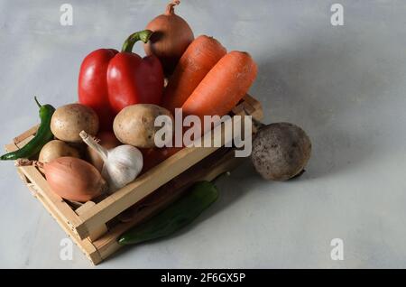 Légumes dans une boîte en bois. Ensemble de légumes, pommes de terre, oignons, ail, poivre, betteraves pour la cuisson du borscht sur fond texturé jaune-gris. Sélection Banque D'Images