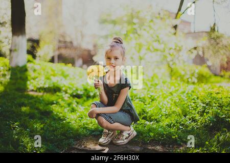 Une fille en robe sniffs un bouquet de pissenlits jaunes dans le jardin de cerisier de printemps Banque D'Images