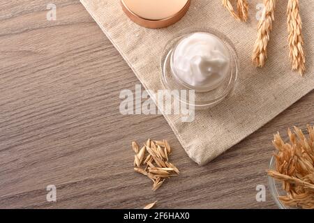 Crème hydratante naturelle avec extrait d'avoine dans un pot en verre toile en toile de jute avec pointes sur table en bois, vue sur le dessus Banque D'Images