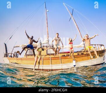 Vue frontale des jeunes amis multiraciaux qui sautent de la voile en bois Excursion en bateau sur la mer - riches gars et filles heureux s'amuser en fête d'été