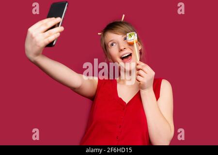 Caucasien jolie femme, blogueur de nourriture faisant photo selfie avec sushi pour le blog.Jolie fille avec un appareil photo de smartphone moderne.Médias sociaux.Monochrome rouge Banque D'Images