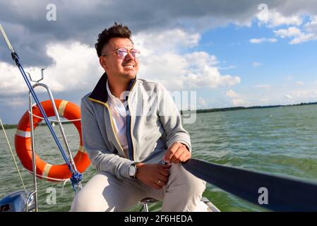 Un jeune homme takin bain de soleil sur un voilier pendant la voile. Vacances d'été à la voile sur un lac Banque D'Images