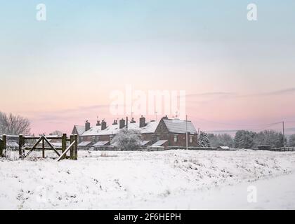 Magnifique coucher de soleil d'hiver sur une rangée de vieilles maisons dans la campagne avec de la neige profonde et un ciel lumineux. La scène enneigée se lève au lever du soleil dans un ciel orange rose Banque D'Images