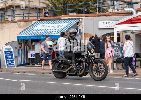 Une femme pilote à bord d'une moto Harley Davidson à Southend on Sea, Essex, Royaume-Uni. En passant par les restaurants Arches de l'Esplanade de l'Ouest. Vêtements noirs Banque D'Images