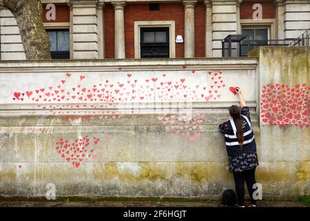 Londres, Royaume-Uni - 31 mars 2021 : la famille et les amis des victimes de Covid-19 peignent des coeurs rouges au mur commémoratif national de Covid, en face de l'hôpital St. Thomas, dans le centre de Londres. Chaque cœur tiré individuellement représente une victime du coronavirus. Banque D'Images