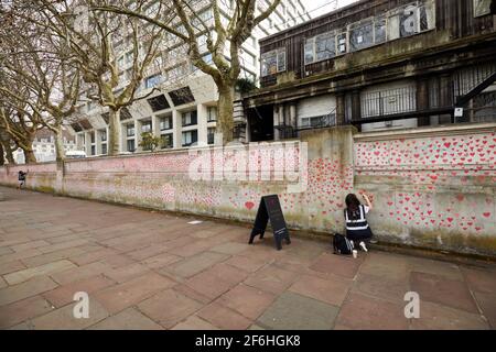 Londres, Royaume-Uni - 31 mars 2021 : la famille et les amis des victimes de Covid-19 peignent des coeurs rouges au mur commémoratif national de Covid, en face de l'hôpital St. Thomas, dans le centre de Londres. Chaque cœur tiré individuellement représente une victime du coronavirus. Banque D'Images