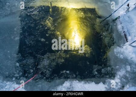Un plongeur sous l'eau brille avec une lampe de poche torche une entrée de trou de glace avec un pour la plongée sous-marine sur glace plongée Banque D'Images