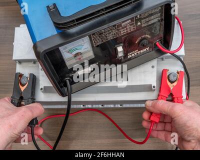 Les mains d’un homme fixent les pinces crocodile rouges et noires d’un chargeur aux bornes positives et négatives d’une batterie de véhicule de 12 volts. Banque D'Images