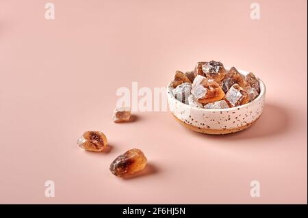 Cubes de sucre de canne caramélisés bruns dans un bol sur fond poudré rose, foyer sélectif, espace de copie Banque D'Images