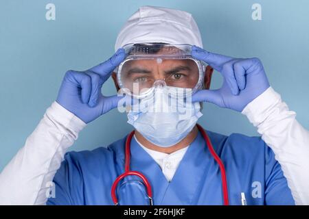 Portrait du médecin portant un masque de protection, des lunettes médicales et un stéthoscope. Image isolée sur fond bleu. Banque D'Images