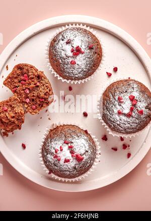 Cupcakes au chocolat faits maison sous forme de papier de cuisson et morceau de celui-ci sur plaque légère sur fond poudreux rose, orientation verticale Banque D'Images