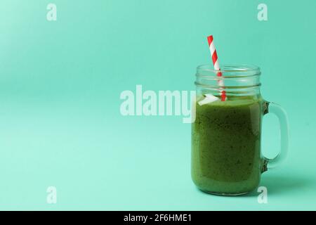 Pot Mason avec un smoothie vert et une paille rayée rouge sur un fond menthe, boisson saine et fraîche avec espace libre Banque D'Images