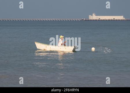 Pêcheur dans un petit bateau tirant dans ses filets, un long quai commercial est en arrière-plan - mer bleu calme par temps clair Banque D'Images