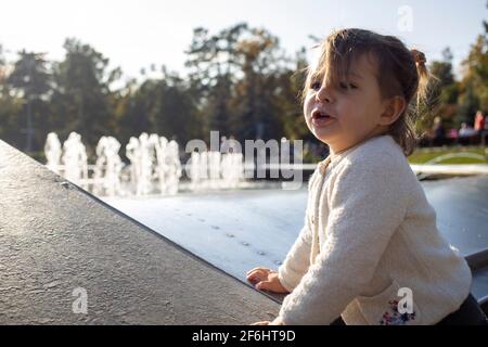 adorable petite fille fait des visages et des grimaces sur fond de parc. l'enfant joue avec gaieté. enfance heureuse Banque D'Images