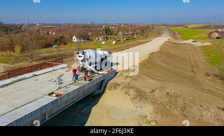 Au-dessus de la vue, les ouvriers du bâtiment répandent et nivelent du béton frais dans une tranchée carrée après avoir versé du camion mélangeur sur le b non fini Banque D'Images