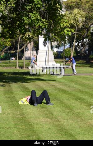 Londres, Angleterre, Royaume-Uni. Homme dans une veste haute visibilité se détendant sur l'herbe dans les jardins Victoria Embankment pendant que deux hommes jouent au tennis de table en extérieur Banque D'Images