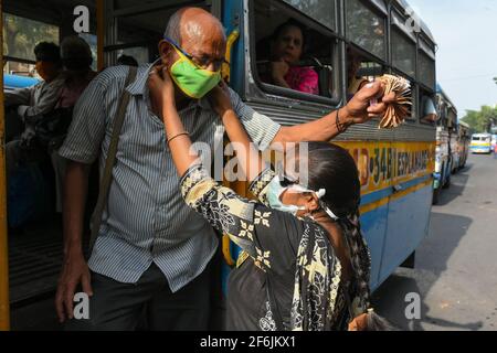 Une fille à l'ablation différente distribuant un masque de protection aux chauffeurs de bus et aux aides dans une rue à Kolkata, en Inde. Banque D'Images