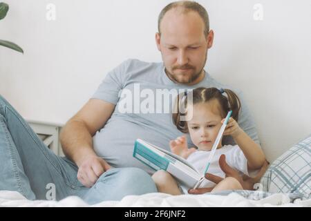 Petite fille 2-4 avec son père assis sur le lit dedans et lit le livre Banque D'Images