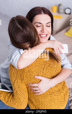 adolescente tenant une tablette numérique et embrassant avec une mère heureuse Banque D'Images