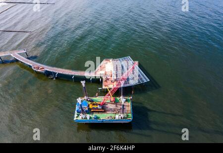 22 mars 2021, Mecklembourg-Poméranie occidentale, Koserow: Un ponton flottant avec une grue se trouve à côté de la nouvelle jetée en construction sur l'île d'Usedom. En raison du remplacement nécessaire de certains bois tropicaux posés comme planches de course et de la galvanisation renouvelée des segments de rampe, le pont ne sera maintenant prêt pour le festival de pont qu'au début de juillet 2021. La jetée s'étend sur près de 300 mètres dans la mer Baltique, et la forme de vague incurvée de la jetée droite sur d'autres ponts est frappante. La nouvelle construction coûtera plus de cinq millions d'euros. (Photo prise avec un drone) photo: Jens Büt Banque D'Images