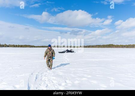 pêcheur transportant un foret et un traîneau. Un homme marche dans la neige profonde et est vêtu d'un costume de camouflage d'hiver. Banque D'Images