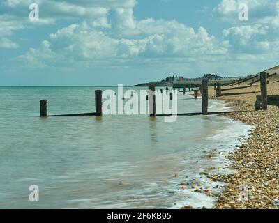 Le long d'une plage passa devant des défenses marines en décomposition, des groynes en bois cassées, avec un affleurement de bâtiments sous un ciel bleu entassé de nuages en coton. Banque D'Images