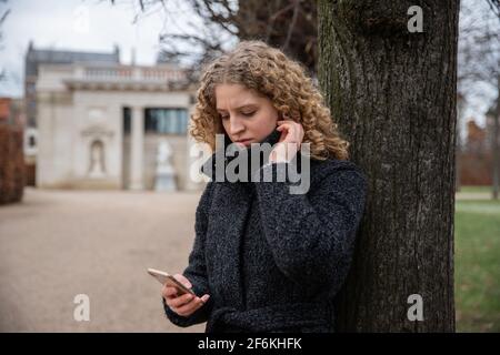 Une adolescente utilise son smartphone avec un visage inquiet pendant une journée d'hiver froide Banque D'Images