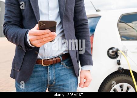 Homme d'affaires utilisant un téléphone portable sur l'arrière-plan de charge de la voiture électrique au point de charge Banque D'Images