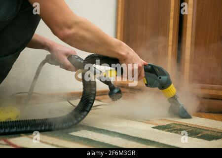 Le processus de nettoyage des tapis avec un aspirateur à vapeur. Un employé d'une entreprise de nettoyage nettoie le tapis à la vapeur. Banque D'Images