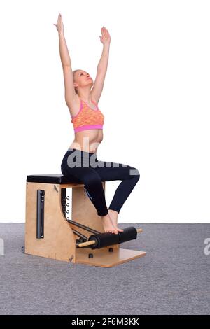 Une formatrice de 20 ans pratique Pilates sur une chaise d'ascenseur, en levant les bras au-dessus de sa tête. Assis. Banque D'Images