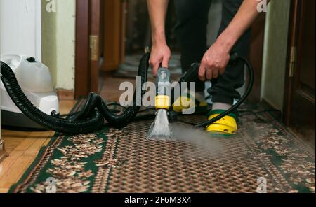 Le processus de nettoyage des tapis avec un aspirateur à vapeur. Un employé d'une entreprise de nettoyage nettoie le tapis à la vapeur. Banque D'Images