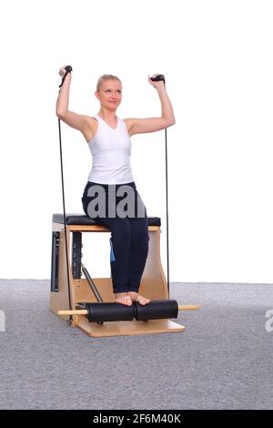 Un entraîneur de 20 ans pratique Pilates sur une chaise d'ascenseur avec l'aide d'un élastique de gymnastique pour son épaule muscles Banque D'Images