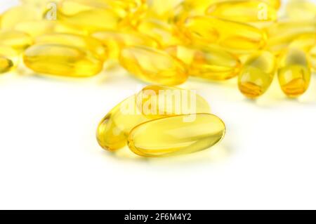 Trois capsules Omega 3 isolées sur fond blanc et beaucoup d'autres capsules sur fond flou. Image macro. Banque D'Images