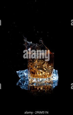 Whisky avec éclaboussures isolé sur fond noir. Scotch avec de la glace dans un verre. Banque D'Images