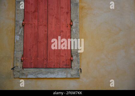 Façade de maison de campagne de style provençal avec un mur en stuc ocre et des volets de fenêtre rouge pâle à Bonnieux Vaucluse, Provence-Alpes-Côte d'Azur France. Banque D'Images
