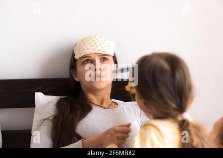 Mignon petite fille portant l'uniforme jouant docteur ou infirmière avec jeune maman ou nounou dans la chambre, fait une injection, mesure la température, dépenses familiales Banque D'Images