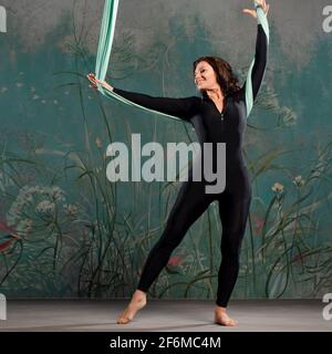 Une belle jeune femme dans un survêtement noir serré fait du yoga sur une suspension, de la gymnastique sur les toiles, des exercices d'équilibre. Banque D'Images