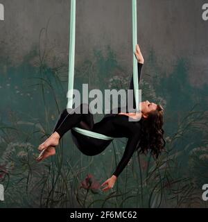 Une belle jeune femme dans un survêtement noir serré fait du yoga sur une suspension, de la gymnastique sur les toiles, des exercices d'équilibre. Banque D'Images