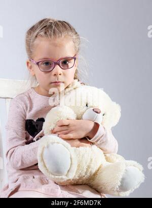 Une fille avec des lunettes pose sur une chaise. Dans les mains d'un ours en peluche blanc. Banque D'Images