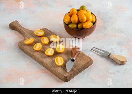 Kumquats entiers dans un bol et kumquats demi-coupés sur bois planche à découper Banque D'Images