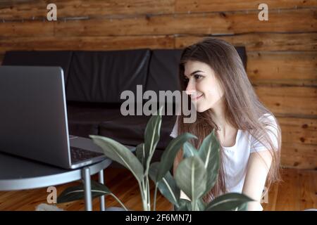 Pensive optimiste femme freelance élève dans une tenue décontractée assis sur le sol et regarder l'écran de l'ordinateur regarder le webinaire ou discussion vidéo Banque D'Images