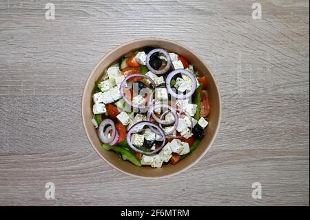 Salade grecque traditionnelle dans un bol placé sur une table en bois avec une vinaigrette grecque maison dans le cadre d'un régime méditerranéen. Banque D'Images