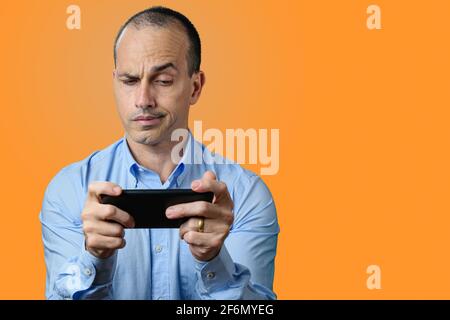 Homme mature en tenue formelle, suspect et regardant son smartphone. Arrière-plan orange. Banque D'Images