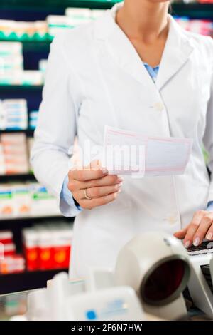 Femme pharmacien en pharmacie, debout à la caissière, elle tient un bordereau d'ordonnance dans ses mains Banque D'Images