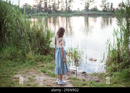 Une fille se tient sur la rive du lac et regarde la nutrition dans l'eau Banque D'Images