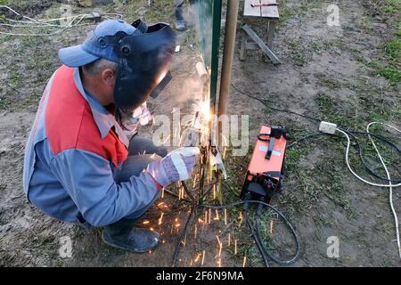 soudage d'un profil métallique à une clôture, procédé de soudage de près, le travailleur dans un casque de protection contre les étincelles.new Banque D'Images