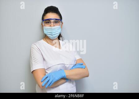 Femme dentiste en uniforme, lunettes de protection et masque facial contre le mur gris Banque D'Images