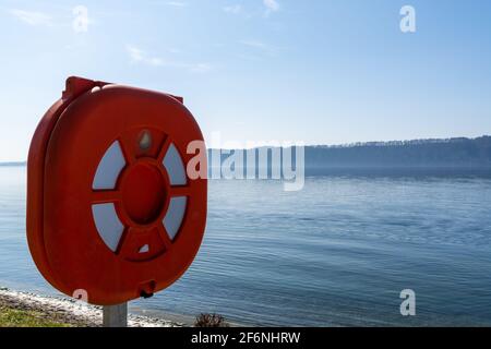 Anneau de sauvetage rouge et station sur les rives d'un lac bleu calme Banque D'Images